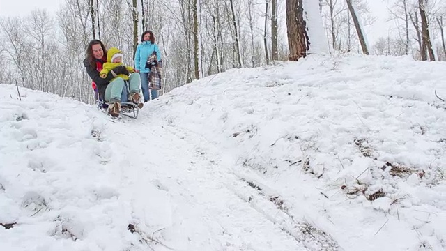 妈妈和一个小女孩骑着雪橇从山上下来视频素材