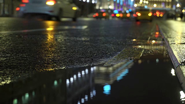 黄色出租车经过后停了下来。汽车和交通灯反射在下雨的道路上视频素材