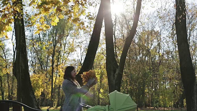 深色头发的妈妈举着一束树叶，在公园里与太阳玩耍。视频素材