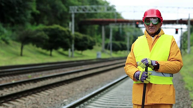 身穿黄色制服、手拿撬棍的铁路工人站在铁路线附近视频素材