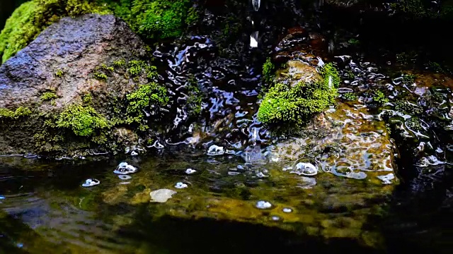 瀑布飞溅的慢镜头近景，泉水下落时，滴落在覆盖着绿色苔藓的岩石上视频素材