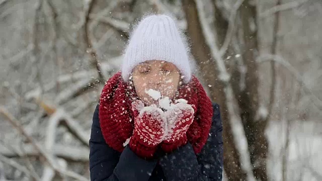 年轻的姑娘戴着白色的针织帽，戴着红色的围巾和手套吹雪视频素材