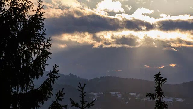 在冬季的时间流逝中，太阳升起在云层和森林景观之上。戏剧性的早晨，树木在风中摇曳视频素材