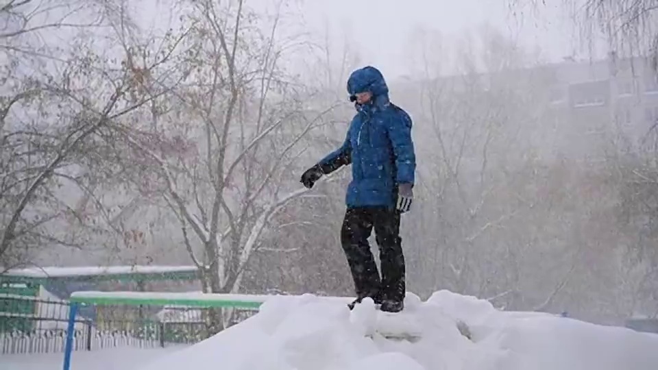 一个孩子跳进冬季公园的雪地里。暴风雪视频素材