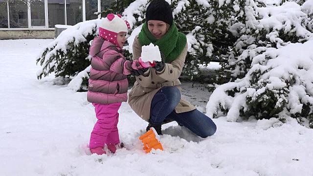 好玩的妈妈和兴奋的女儿一起建造雪城堡，并摧毁它视频素材