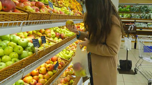 女人在杂货店的农产品部门挑选新鲜的红苹果，并把它放在塑料袋里。年轻漂亮的女孩正在超市挑选苹果，并把它们放进购物篮。近距离视频素材