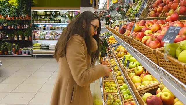 女人在杂货店的农产品部门挑选新鲜的红苹果，并把它放在塑料袋里。年轻漂亮的女孩正在超市挑选苹果，并把它们放进购物篮。近距离视频素材