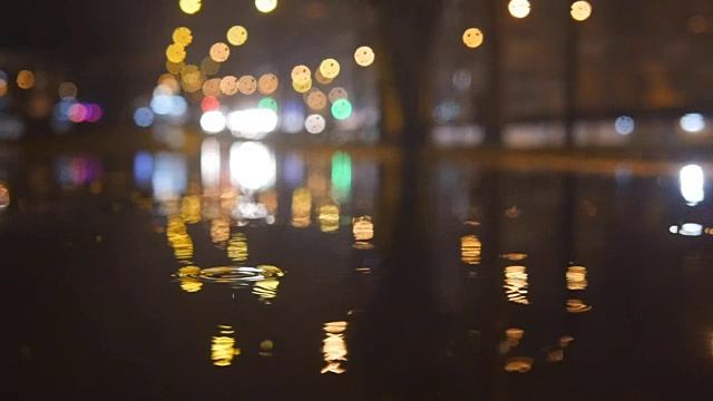 慢动作灯光散景在水中倒映在夜晚的城市街道上的小雨滴视频素材