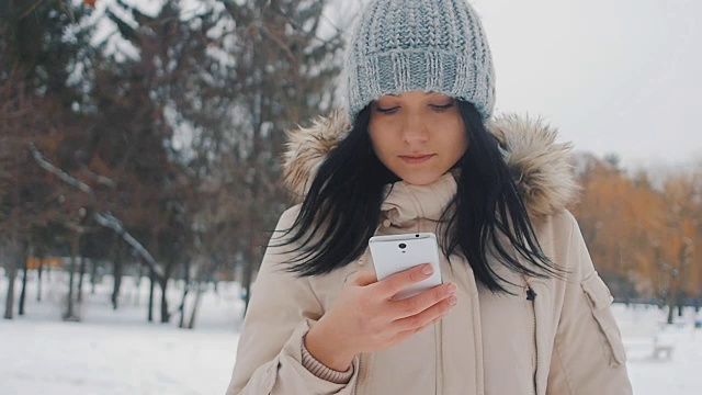 肖像的年轻可爱的女人在冬季公园使用智能手机视频素材