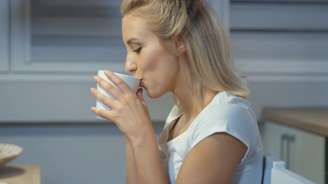 快乐的年轻女人在厨房里拿着杯子。视频素材