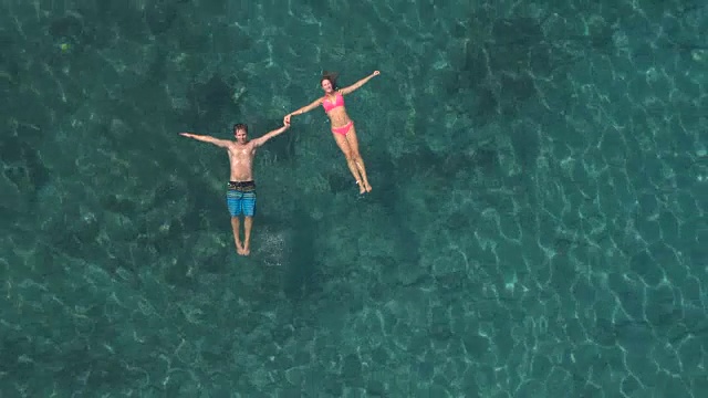 天线:微笑的情侣在海里游泳，手牵着手漂浮在水面上视频素材