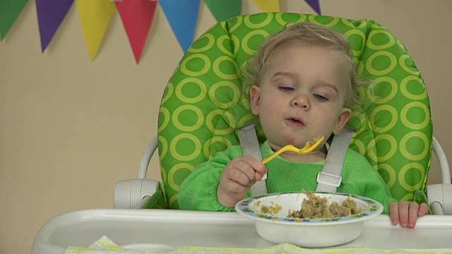 独立的小男孩用勺子坐在喂食椅上吃粥视频素材