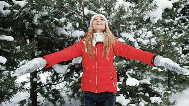 金发微笑的女人把雪扔在冬天的松林外面视频素材