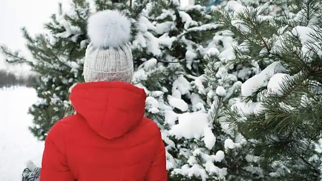 一个美丽的女人愉快地走在白雪覆盖的针叶树下视频素材