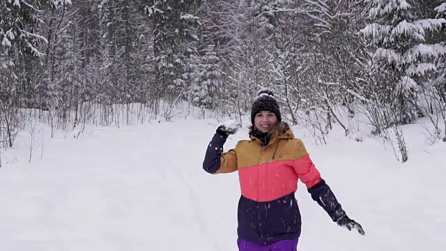 年轻快乐的女人穿着鲜艳的冬装在冬天的森林里扔雪球。视频素材