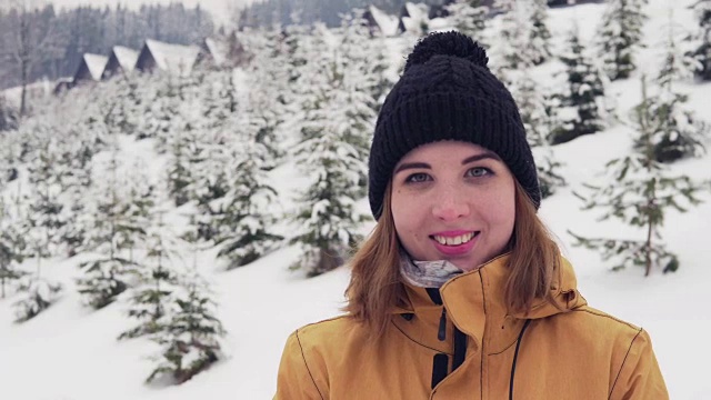 年轻女子穿着鲜艳的冬装站在外面。白雪森林的背景。视频素材