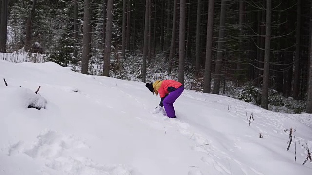 年轻快乐的女人穿着鲜艳的冬装在冬天的森林里扔雪球。视频素材