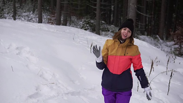 年轻快乐的女人穿着鲜艳的冬装在冬天的森林里打雪仗和扔雪球。视频素材