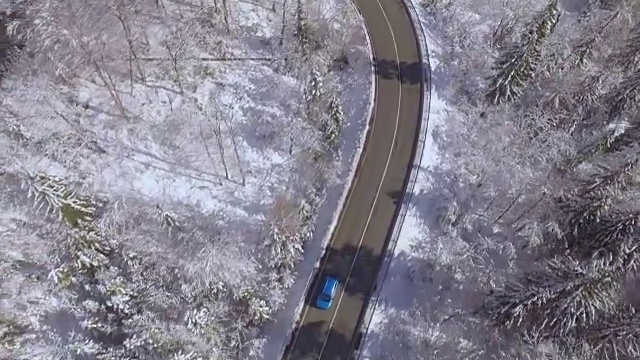 航拍:蓝色的汽车在充满魔力的冰雪仙境中沿着陡峭的弯道行驶视频素材