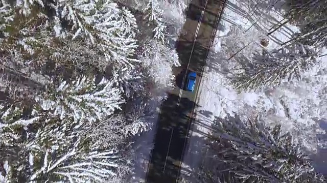 在美丽的雪山森林里，蓝色的汽车在狭窄的道路上行驶视频素材