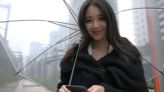 亚洲女性在雨中使用智能手机发短信视频素材