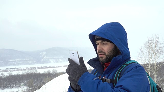 在山上用智能手机玩胡子的游客。穿夹克的白种人在寻找GPS信号。登山者冬季移动通信。探险探险人会说话的细胞人称为意外视频素材