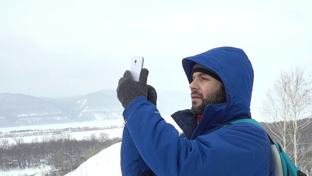 在山上用智能手机玩胡子的游客。穿夹克的白种人在寻找GPS信号。登山者冬季移动通信。探险探险人会说话的细胞人称为意外视频素材