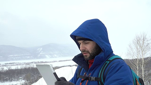 有胡子的旅行者在山上使用平板电脑。穿夹克的白种人在寻找GPS信号。登山者冬季移动通信。探险探险人谈话细胞人呼叫事故视频素材