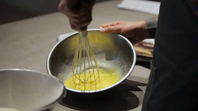 一个年轻人搅拌鸡蛋和面粉做馅饼。一个男人在为现代厨房准备蛋糕视频素材