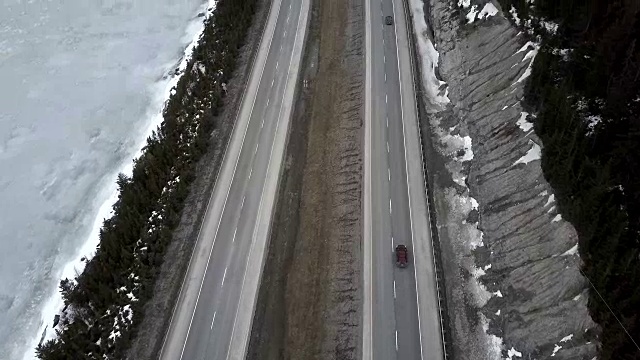 空中的四车道高速公路在落基山脉旁边的一个冰冻的湖冬天视频素材