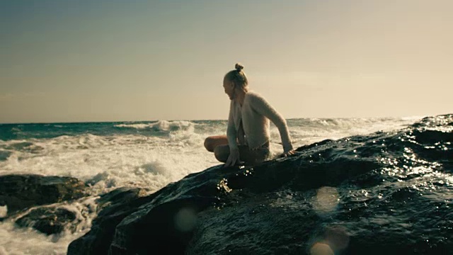 浪花溅在坐在岩石上的年轻女孩身上视频素材