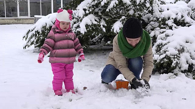 女人带着女儿扔雪球。幸福的家庭的女孩。雪落视频素材