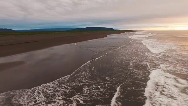 航空摄影机镜头。在日落时沿着海滩相机飞行。美丽的青山景色。视频素材