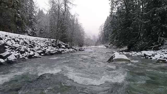 冬季雪花落在无人机上的慢动作飞行低飞过高山森林河流急流视频素材