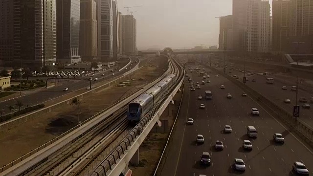 从空中俯瞰蓝色的高速列车，它穿过高速公路上的立交桥，汽车被摩天大楼包围。迪拜,阿联酋视频素材