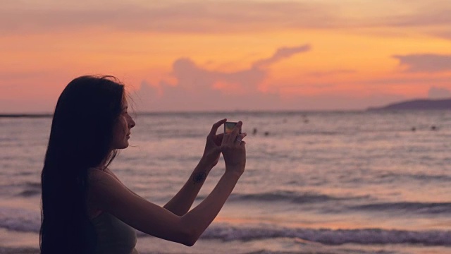 年轻的女游客在海滩上用智能手机拍摄海景视频素材