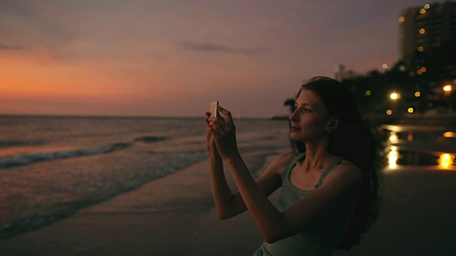 年轻的女游客在海滩上用智能手机拍摄海景视频素材