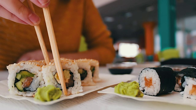 女孩坐着用木棒在咖啡馆的桌子上拿着一个寿司是寿司，日本料理视频素材