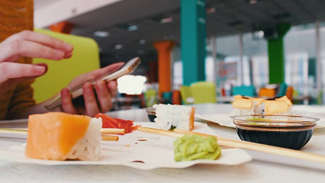 女孩坐在智能手机上打字，和对话者在咖啡馆的桌子上交流寿司，日本料理视频素材