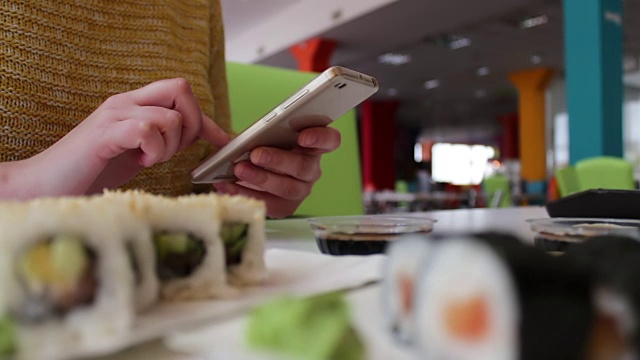 女孩坐在智能手机上打字，和对话者在咖啡馆的桌子上交流寿司，日本料理视频素材