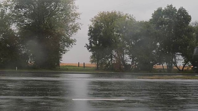 视野中的汽车在雨中驶过，四处溅起水花。另一边有树视频素材