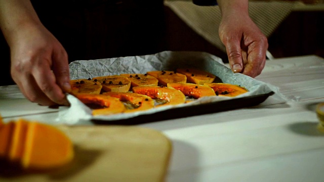 男人的手拿着南瓜片放在烤盘上。食谱烤南瓜视频素材