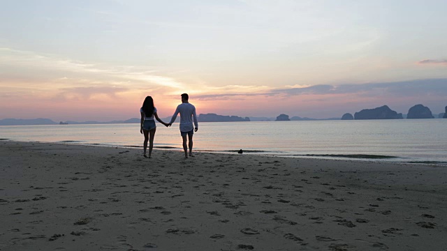 海滩上的情侣在日落时牵手，浪漫的男人和女人游客视频素材