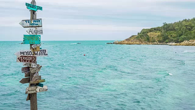 热带岩石海滩的木制路标，海浪和长尾船的背景视频素材