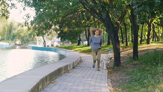 年轻的女性和拉布拉多猎犬在公园里奔跑，慢镜头视频素材