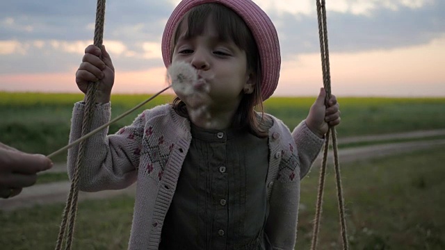 吹蒲公英，画可爱的小女孩在荡秋千，女孩子在吹花球，快乐的孩子在大自然中视频素材