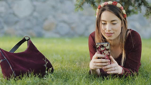 美丽的女人躺在草地上玩手机视频素材