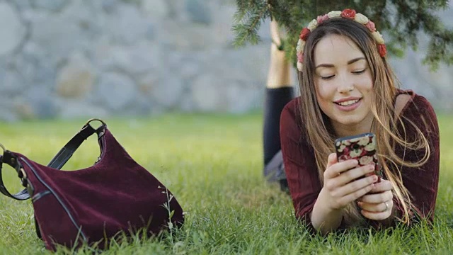 美丽的女人躺在草地上玩手机视频素材