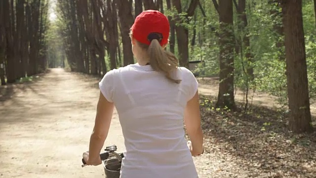 快乐活跃的年轻女子在红帽自行车通过阳光灿烂的公园在夏天的一天视频素材