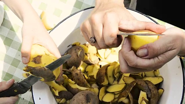 女人的手用菜刀削鲜黄土豆的细节。在外面的花园里。准备食物的概念。视频素材